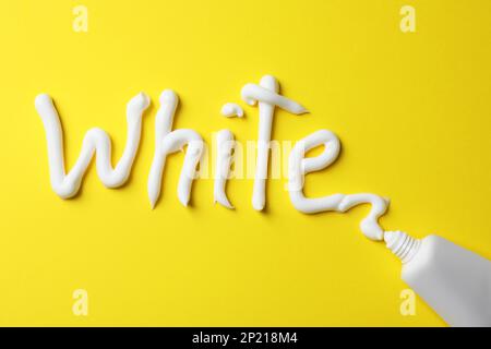 Word White scritto con dentifricio e tubo su sfondo giallo, vista dall'alto Foto Stock