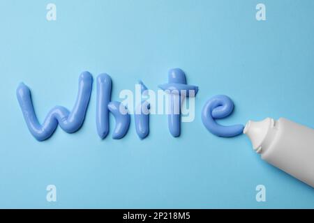 Word White scritto con dentifricio e tubo su sfondo azzurro, piatto Foto Stock