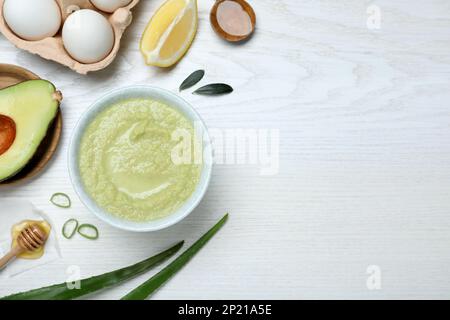 Maschera fatta in casa in ciotola e ingredienti su tavolo di legno bianco, piatto. Spazio per il testo Foto Stock