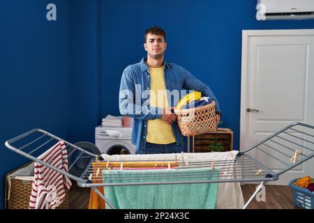 Giovane uomo ispanico appendere abiti a clothesline pensiero atteggiamento e sobrio espressione guardando sicuro di sé Foto Stock