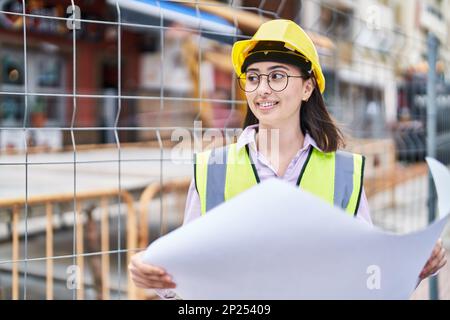 Giovane donna ispanica architetto lettura piani in strada Foto Stock