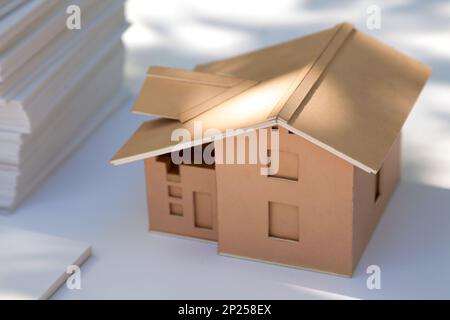 Piccolo modello di casa di cartone su bianco. Nuovo design per la casa in vendita. Astratto cartone immobiliare in miniatura alla luce del sole Foto Stock