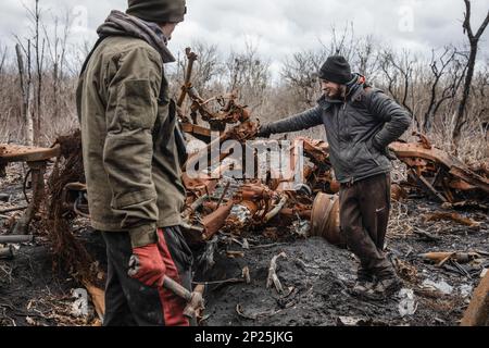 Gli uomini locali smantellano i resti di attrezzature militari russe distrutte e bruciate per rottami metallici, regione di Kharkiv, Ucraina. Guidando lungo le strade della regione di Kharkiv, più vicino si arriva a Donbas, le attrezzature militari più bruciate e rotte che si vede sul lato della strada, nei campi e nelle cinghie forestali. In uno di questi nastri forestali abbiamo visto una grande quantità di apparecchiature russe bruciate. Quando abbiamo smesso di scattare foto, abbiamo visto diversi uomini e adolescenti che si rimesero sistematicamente. Stavano smontandolo per i rottami di metallo, per i quali ricevono 2 crivnie per chilogrammo. Non possono raccogliere più t Foto Stock