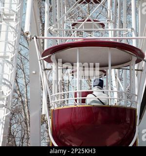 Ragazza triste su una ruota panoramica al parco di divertimenti, il freddo invernale depressione. Donna sulla ruota di osservazione ride cabina vicino alla fiera Foto Stock