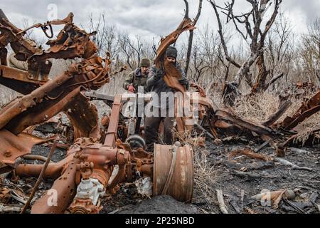 Gli uomini locali smantellano i resti di attrezzature militari russe distrutte e bruciate per rottami metallici, regione di Kharkiv, Ucraina. Guidando lungo le strade della regione di Kharkiv, più vicino si arriva a Donbas, le attrezzature militari più bruciate e rotte che si vede sul lato della strada, nei campi e nelle cinghie forestali. In uno di questi nastri forestali abbiamo visto una grande quantità di apparecchiature russe bruciate. Quando abbiamo smesso di scattare foto, abbiamo visto diversi uomini e adolescenti che si rimesero sistematicamente. Stavano smontandolo per i rottami di metallo, per i quali ricevono 2 crivnie per chilogrammo. Non possono raccogliere più t Foto Stock