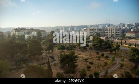 Il paesaggio urbano di Ramallah all'alba con tramonto, alti edifici e alberi di fronte al sole Foto Stock