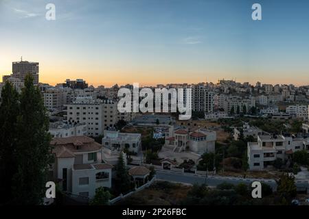 Ramallah, Ramallah e al-Bireh Governatorato, Palestina, 8 luglio 2022: Ramallah paesaggio urbano al tramonto con alti edifici e alberi contro giallo scuro e. Foto Stock