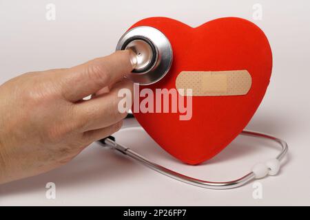 donna che auscultava un cuore rosso con un cerotto con uno stetoscopio isolato su sfondo bianco Foto Stock