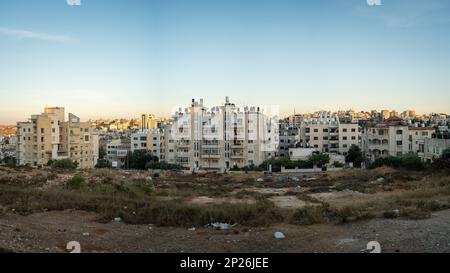 Il paesaggio urbano di Ramallah al tramonto con edifici in pietra bianca alta e macchie di erba Foto Stock