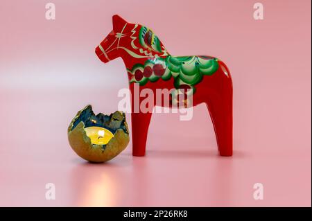 Una scena natalizia scandinava con un Cavallo di legno di Dala rosso svedese e una candela illuminata su uno sfondo rosa Foto Stock