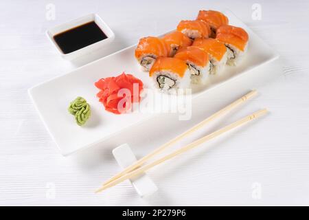 Filadelfia di sushi con salmone, anguilla affumicata, avocado, formaggio cremoso su sfondo bianco. Menu di sushi, panini serviti su piatto bianco con wasabi, zenzero Foto Stock