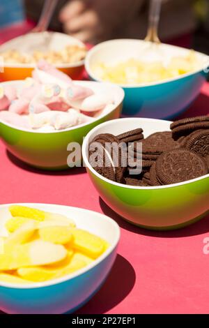 Chocolate cookies, marshmallows and other confectionery in bright bowls.  Fun colorful close-up of various types of sweets. Tasty snacks at birthday b Stock Photo