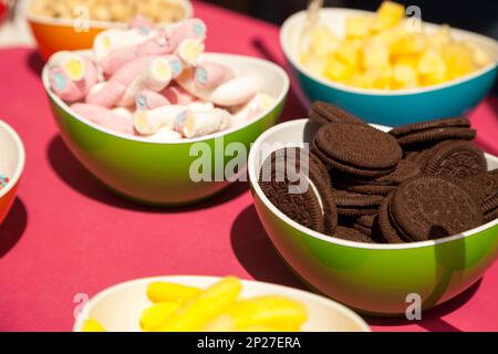 Chocolate cookies, marshmallows and other confectionery in bright bowls.  Fun colorful close-up of various types of sweets. Tasty snacks at birthday b Stock Photo