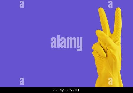 Mani dei pulitori in guanto giallo con segno di vittoria, simbolo V con le dita. Sfondo del banner con spazio di copia per il testo. Foto Stock