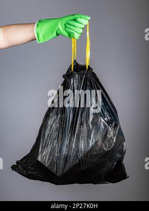 Mano in guanto impugnature di plastica nera sacchetto usa e getta pieno di rifiuti, rifiuti, rifiuti. Concetto di pulizia della casa, decluttering. Foto Stock