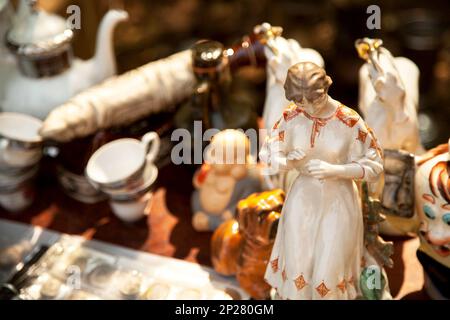 Porcellana antica donna e altre figurine e stoviglie presso il mercato delle pulci . Vecchia ragazza di ceramica statuetta e Cina vasellame collectibles presso il garage Foto Stock