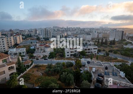 Ramallah, Ramallah e al-Bireh Governatorato, Palestina, 13 luglio 2022: Ramallah città paesaggio all'alba con tramonto, alti edifici, e alberi di fronte al sole Foto Stock