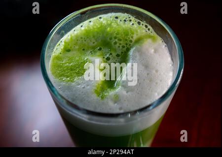 Bicchiere di tè Matcha verde fatto da polvere finemente macinata di foglie di tè verde appositamente coltivate e lavorate consumate nell'Asia orientale con latte caldo montato Foto Stock