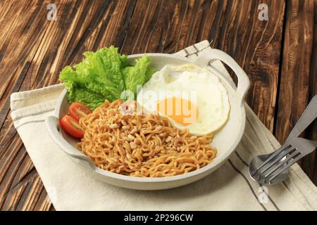 Indomie Goreng o mie Goreng, indonesiano popolare Instant Noodle. Servito con uovo di lato soleggiato, pomodoro, cetriolo. Foto Stock