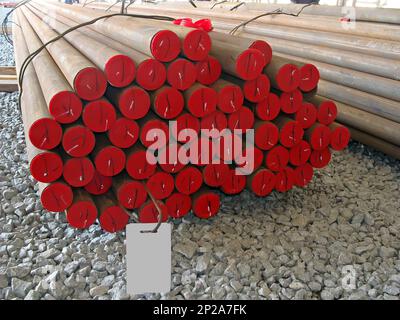 Impilamento di tubi in acciaio senza saldatura in cantiere. Tappi rossi sulle estremità dei tubi tondi. Foto Stock