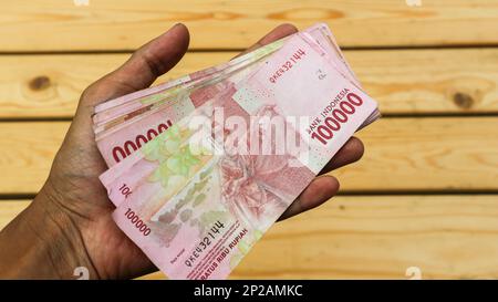 La mano di un uomo tiene centomila rupiah nota. Foto Stock