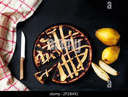 torta e pere sono disposti su uno sfondo nero accanto a un asciugamano da cucina Foto Stock