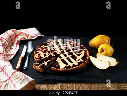 torta e pere sono disposti su uno sfondo nero accanto a un asciugamano da cucina Foto Stock