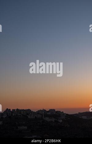 Ramallah Arab Town costruzione di silhouette su una collina lontano in un deserto contro il cielo crepuscolo di colore chiaro Foto Stock