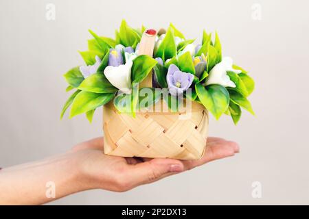 Un piccolo cesto di impiallacciatura con croccoli e narcisi in sapone fatto a mano su una mano di donna. Foto Stock