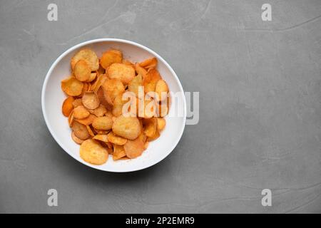 Patatine Cassava organiche in ciotola bianca su fondo grigio. Indonesia popolare spuntini piccanti caldi. Keripik singkong. Vista dall'alto. Spazio di copia. Foto Stock