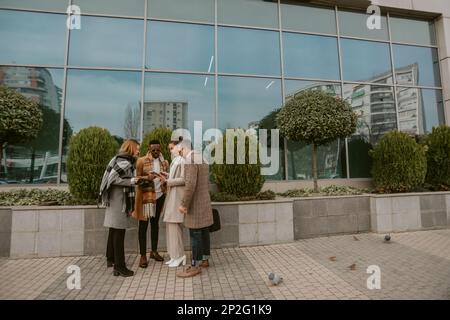 Quattro colleghi aziendali che lavorano sul tablet mentre si trovano all'esterno di fronte all'edificio Foto Stock