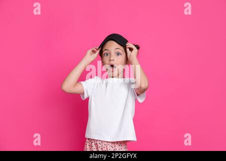 Ragazza carina in pigiama con maschera di sonno su sfondo rosa Foto Stock