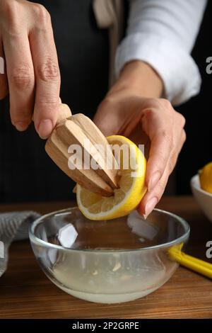 Donna spremitura succo di limone con spremiagrumi a tavola di legno, primo piano Foto Stock