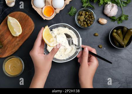 Donna che aggiunge succo di limone alla salsa tartare al tavolo nero, vista dall'alto Foto Stock