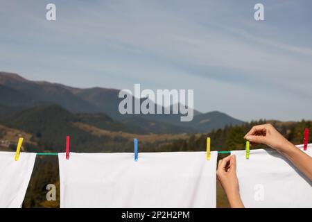 Donna che mette i perni di vestiti sulla linea di lavanderia all'aperto, closeup. Spazio per il testo Foto Stock