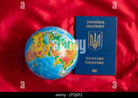 Globo e passaporto biometrico ucraino straniero su sfondo rosso, viaggio Foto Stock