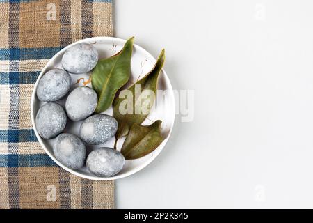 Uova di Pasqua grigie con un rametto e una foglia di magnolia su sfondo grigio. Minimalismo, spazio copia, giacitura piatta Foto Stock