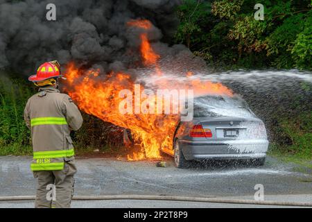 Saint John, NB, Canada - 18 agosto 2022: Una macchina parcheggiata inghiottita in fiamme. Un flusso di acqua schiumosa combatte il fuoco come un vigile del fuoco. Foto Stock