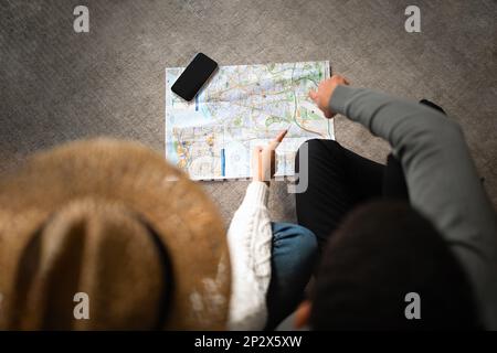 Donna europea millenaria, arabo maschio guardando la mappa, scegliendo il paese per le vacanze sul piano con smartphone Foto Stock