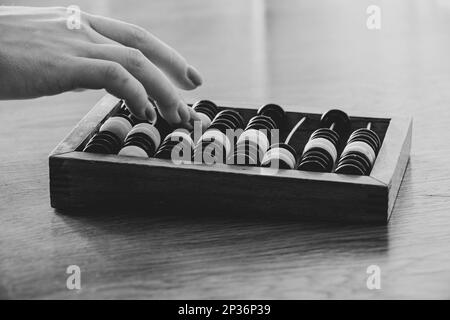 Vecchio abaco di legno per contare i soldi su un tavolo di legno e la mano di una donna conta sull'abaco, foto ravvicinata in bianco e nero Foto Stock