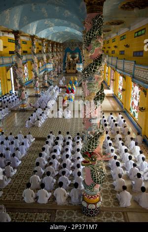 I discepoli di Caodaist seduti accanto a colonne colorate con draghi durante la cerimonia, il tempio di Cao dai, la Santa sede di Tay Ninh, Tay Ninh, Provincia di Tay Ninh Foto Stock