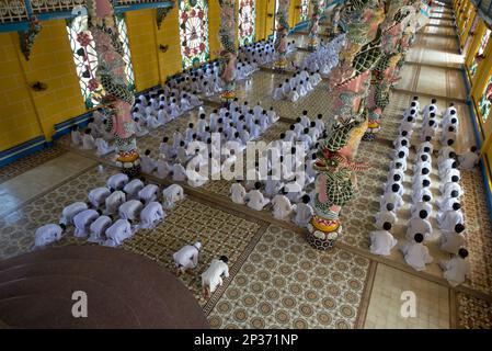 I discepoli di Caodaist seduti accanto a colonne colorate con draghi durante la cerimonia, il tempio di Cao dai, la Santa sede di Tay Ninh, Tay Ninh, Provincia di Tay Ninh Foto Stock