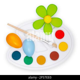 Tavolozza di colori con pennelli, fiori e uova colorate, vista dall'alto isolata su sfondo bianco. Decorazioni pasquali: Portare gioia e Cheer al vostro Foto Stock