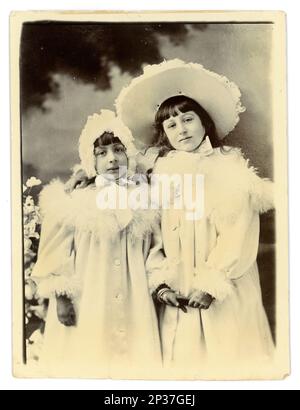Originale fotografia vittoriana di 2 giovani ragazze sorridenti, fratelli, in camici bianchi rifiniti con piume di struzzo, cofani e cappello coordinati, indossando guanti. Circa 1898, area di Worcester, Regno Unito Foto Stock