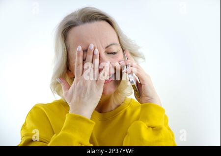 notizie inaspettate donna parla al telefono coprendo gli occhi con la mano sorridendo alla sua vergognosa situazione di comunicazione imbarazzo modestia donna di mezza età luminosa emozioni primo piano Foto Stock