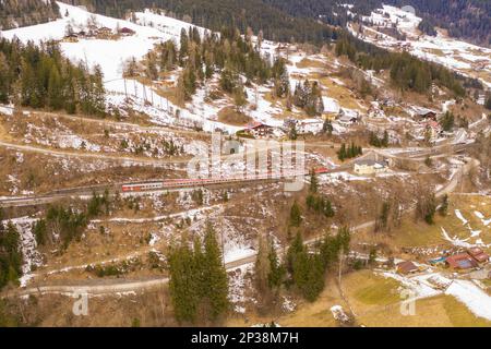 Fotografia del drone di ferrovia che va sopra la montagna e treno durante il giorno nuvoloso di inverno Foto Stock