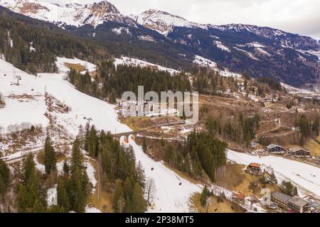 Fotografia in drone del pendio del cielo di montagna, del ponte ferroviario che va sopra il pendio e degli impianti di risalita del cielo durante la giornata nuvolosa di inverno Foto Stock