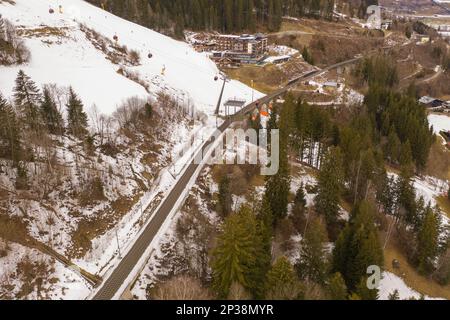 Fotografia in drone del pendio del cielo di montagna, del ponte ferroviario che va sopra il pendio e degli impianti di risalita del cielo durante la giornata nuvolosa di inverno Foto Stock