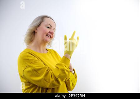 Guanti per la casa gialli e spugna di melammina bianca su sfondo blu. Utensile universale per la pulizia di varie superfici da sporco e macchie casalinga indossa guanti gialli in lattice Foto Stock