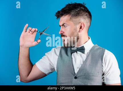 Barbiere con barba e baffi tenere forbici in acciaio. Rifinitura della barba. Crea il tuo stile. Macho barbiere bearded tenere forbici taglio capelli. Servizio di barbiere Foto Stock